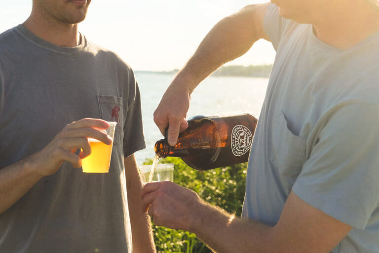 Two gentlemen pouring out some delicious Great Flats beer from a growler while the sun sets