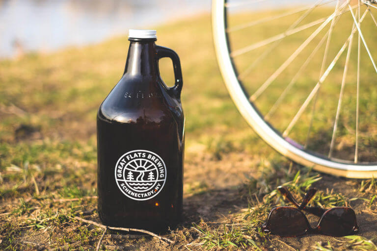 A 32 ounce Great Flats growler full of delicious beer next to a bicycle